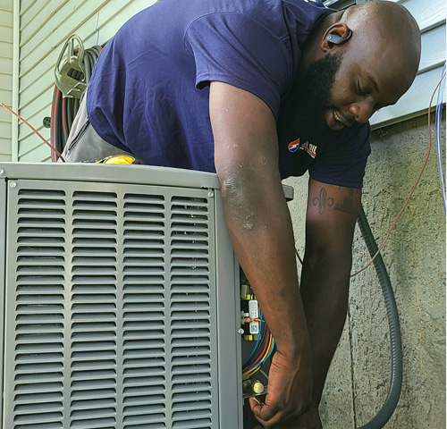 Hometown Heating technician checking refrigerant connections on AC compressor
